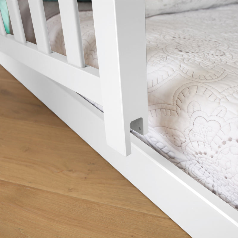Max and Lily Add on Safety Guard Rail in White - close-up of the rail post and metal bracket attaching to the bed frame above a wood floor.