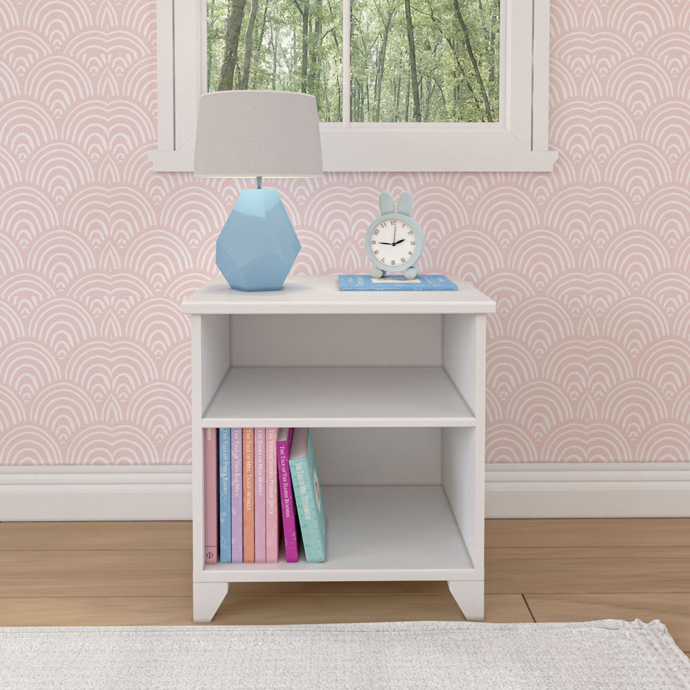 Max and Lily Classic Night Stand With Shelves in White - front view against pink wallpaper with a lamp and books on the shelves.
