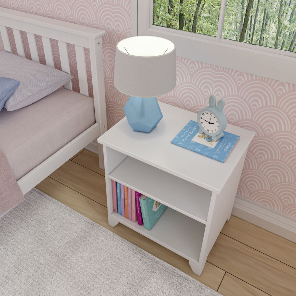 Max and Lily Classic Night Stand With Shelves in White - overhead view beside a bed with a lamp, clock, and books in a child's bedroom.