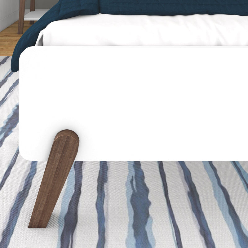 Max and Lily Mid-Century Modern Full Bed in White/Walnut - closeup of the footboard panel and angled walnut leg over a striped area rug