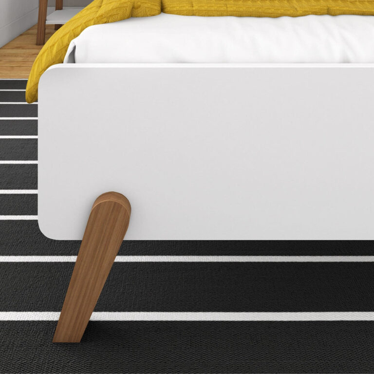 Max and Lily Mid-Century Modern Twin Bed in White/Pecan - closeup of the white footboard corner and splayed pecan wood leg on a striped rug
