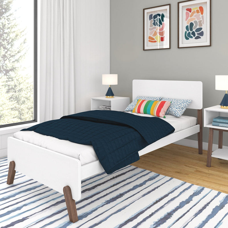 Max and Lily Mid-Century Modern Twin Bed in White/Walnut - angled view in a styled bedroom with navy quilt, colourful pillows, nightstands and a striped rug
