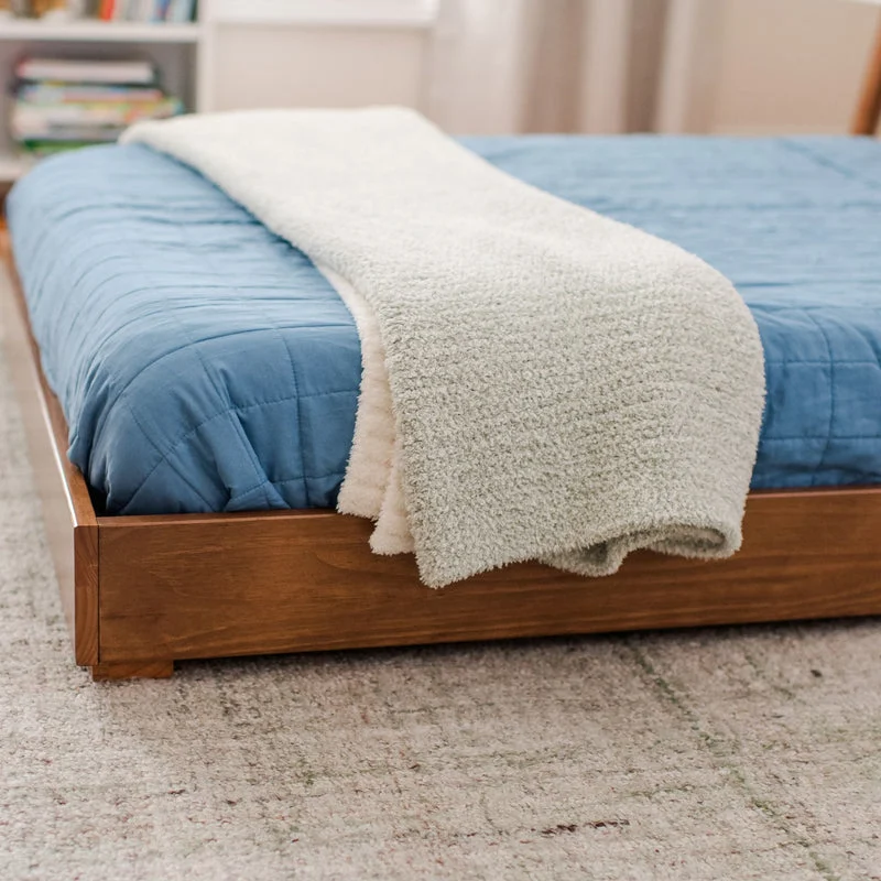 Max and Lily Mid-Century Modern Twin Floor Bed in White/Pecan - closeup of the solid wood frame corner and low platform edge beside a blue quilt