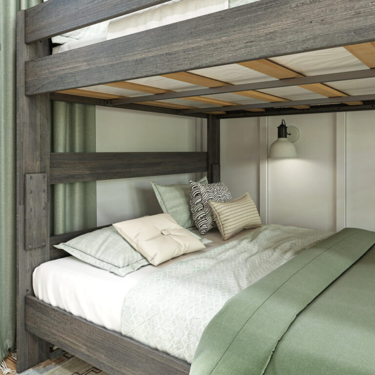 Max And Lily Modern Farmhouse Queen Over Queen Bunk Bed Driftwood Lower Bunk Detail Max and Lily Modern Farmhouse Queen Over Queen Bunk Bed in Driftwood - close-up of the lower bunk styled with sage green and cream pillows beside a lit wall sconce