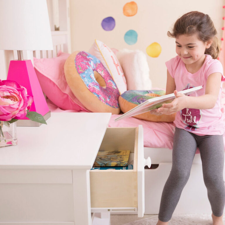 Max And Lily Night Stand With Drawer And Shelf White Child Reading Max and Lily Night Stand With Drawer and Shelf in White - a girl reads on the bed beside the nightstand with its drawer open holding books.