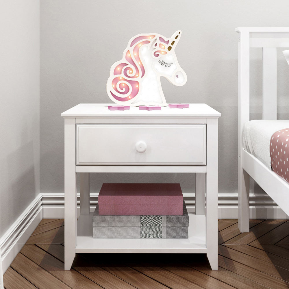 Max and Lily Night Stand With Drawer and Shelf in White - shown in a child's room with a unicorn lamp on top and books stacked on the lower shelf next to a bed.