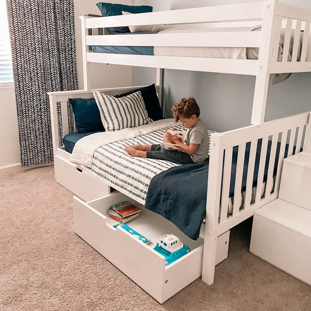 Max and Lily Twin Over Full Bunk Bed with Stairs and Storage in White - a boy reading on the lower full bunk with an under-bed storage drawer pulled open.