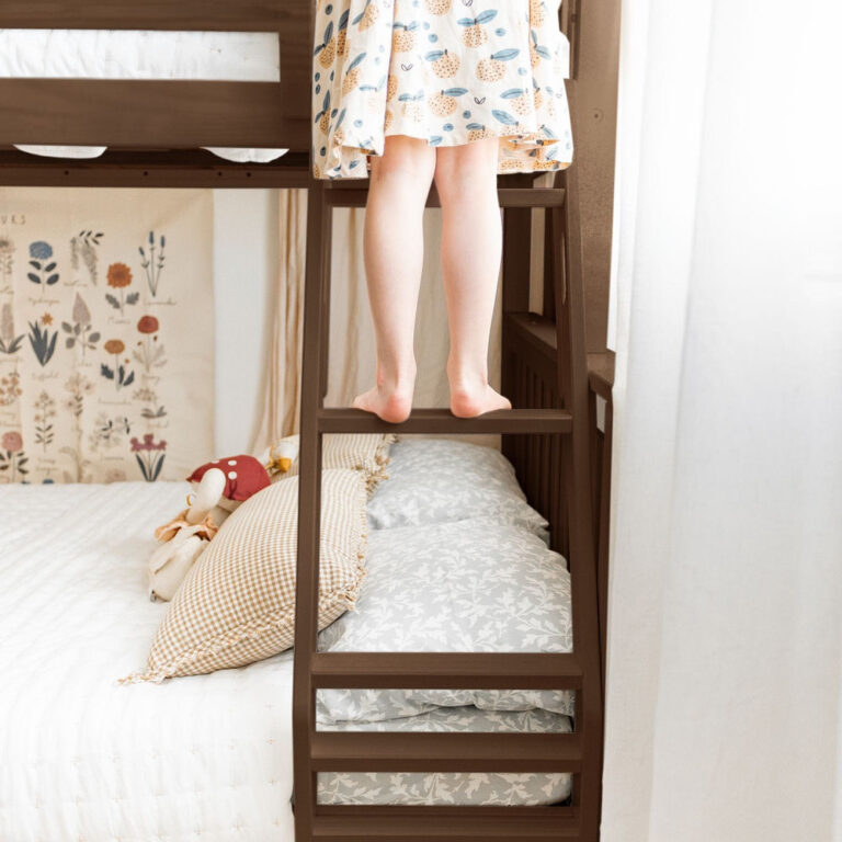 Max and Lily Twin Over Full Bunk Bed with Trundle in Walnut - child standing barefoot on the wide angled ladder steps above the full lower bunk