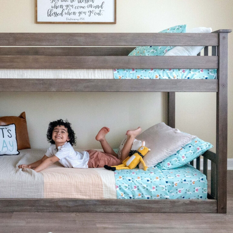 Max And Lily Twin over Twin Low Bunk Bed in clay - smiling child lying on the bottom bunk with a plush toy, showing the low overall height and sturdy rails