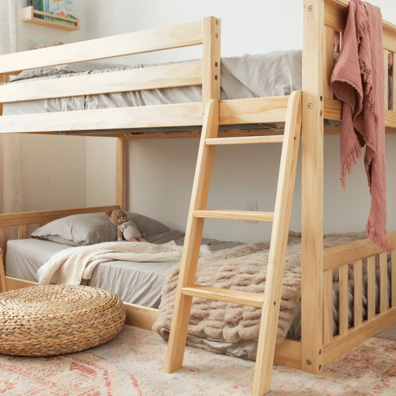 Max And Lily Twin over Twin Low Bunk Bed in Natural - low bunk with safety guardrails and angled ladder styled in a kids room with a woven pouf and area rug