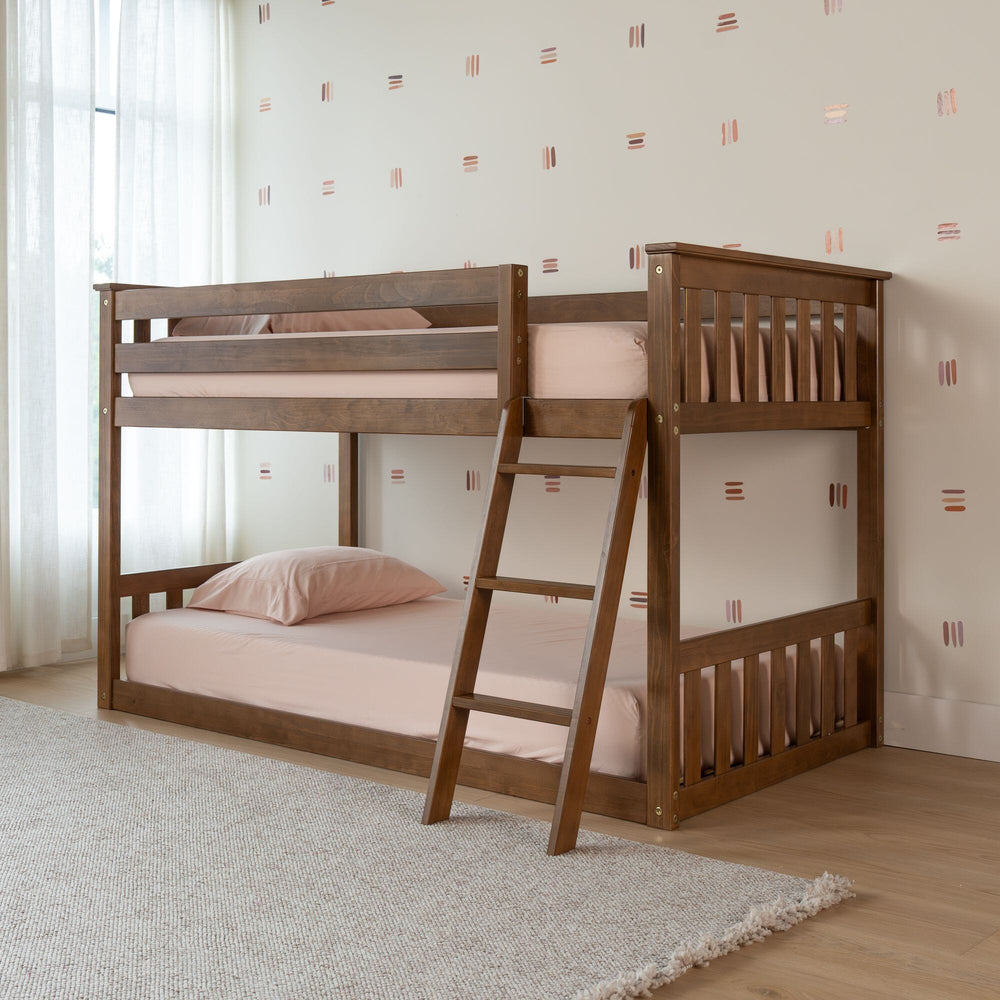 Max And Lily Twin over Twin Low Bunk Bed in Pecan - angled view in a kids bedroom with pink bedding, full-length safety guardrails and an angled access ladder