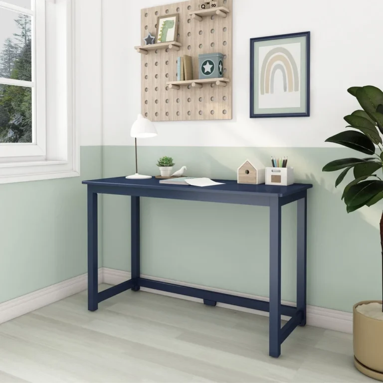 Max and Lily Writing Desk in Blue - angled view in a kids room beside a window, with a desk lamp, plant, and rainbow wall art.