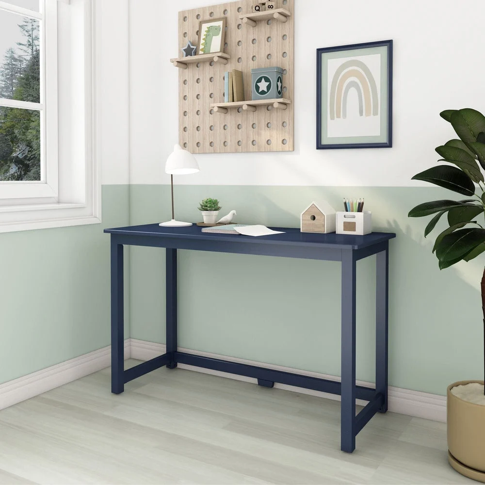 Max and Lily Writing Desk in Blue - angled view in a kids room beside a window, with a desk lamp, plant, and rainbow wall art.