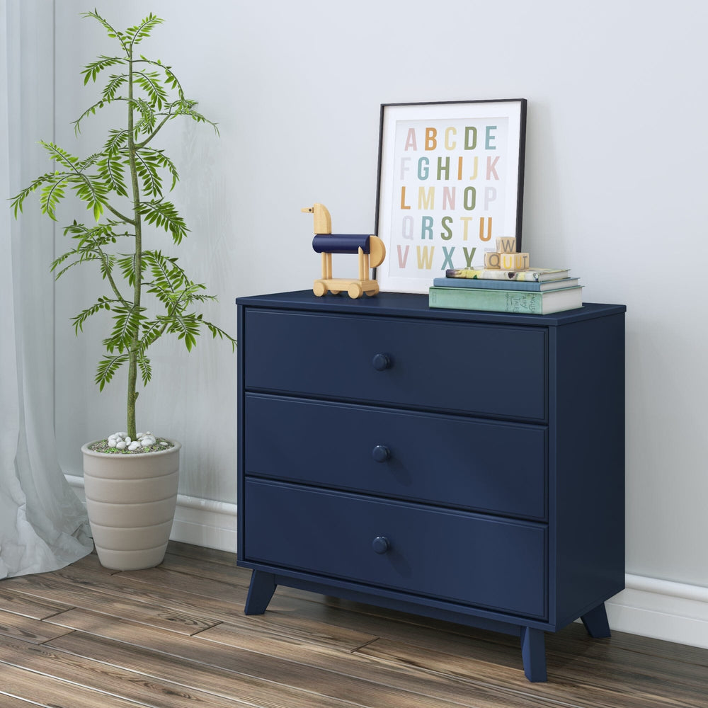 Max & Lily Classic 3 Drawer Dresser in Blue - styled at an angle in a child's room beside a potted plant, alphabet art print, and a wooden toy dog.