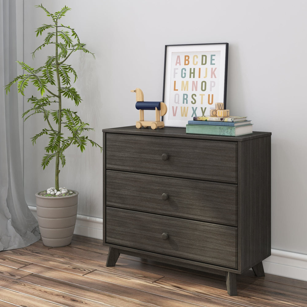 Max & Lily Classic 3 Drawer Dresser in Clay - angled in a styled kids room with a potted plant, framed alphabet print and wooden dog toy displayed on top.