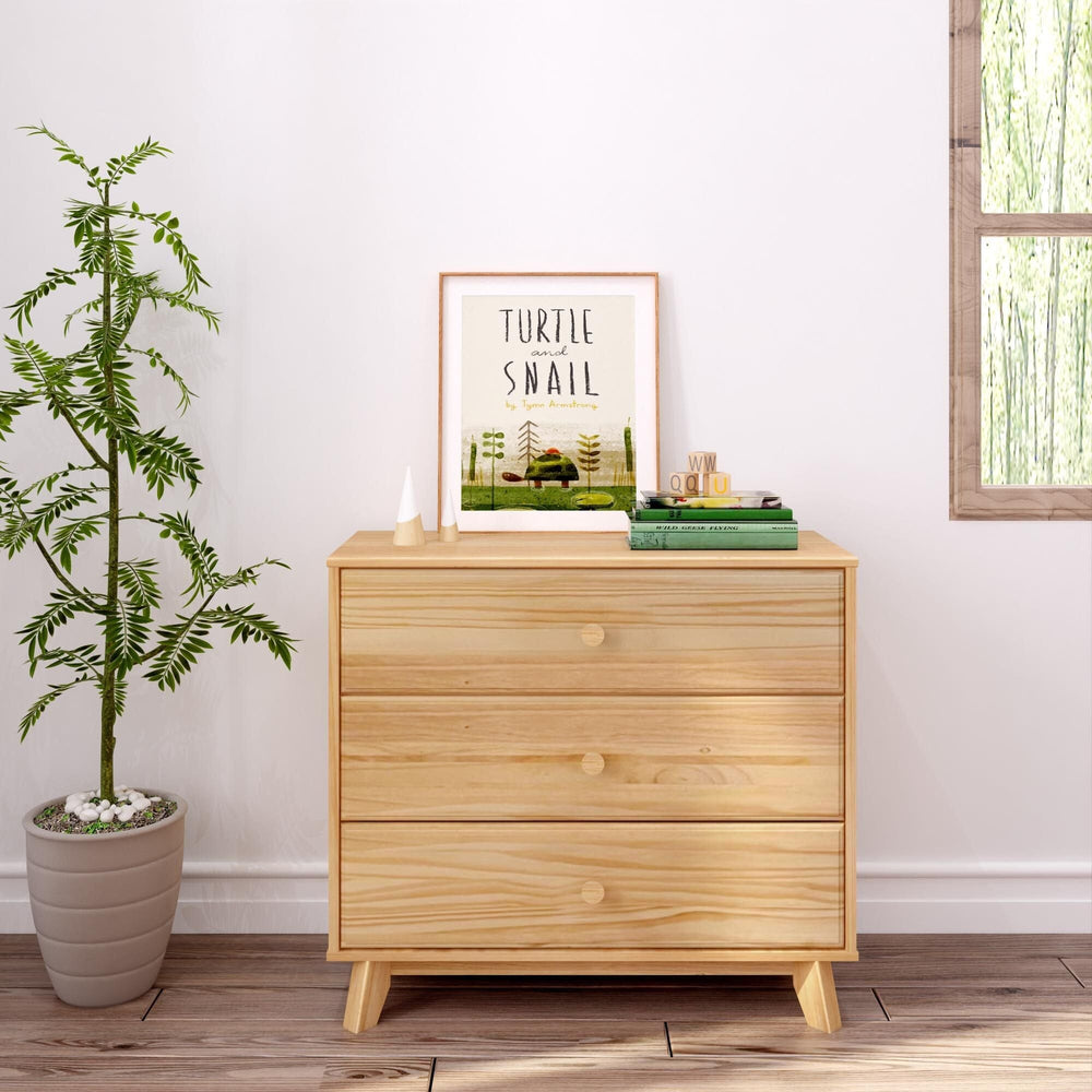 Max & Lily Classic 3 Drawer Dresser in Natural - front view styled in a bedroom next to a plant with framed art on top