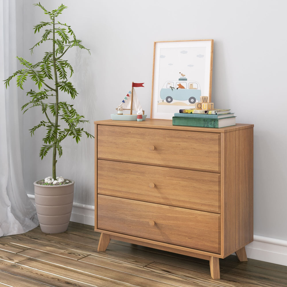 Max & Lily Classic 3 Drawer Dresser in Pecan - styled in a child's room with a potted plant, framed art print, and books on top