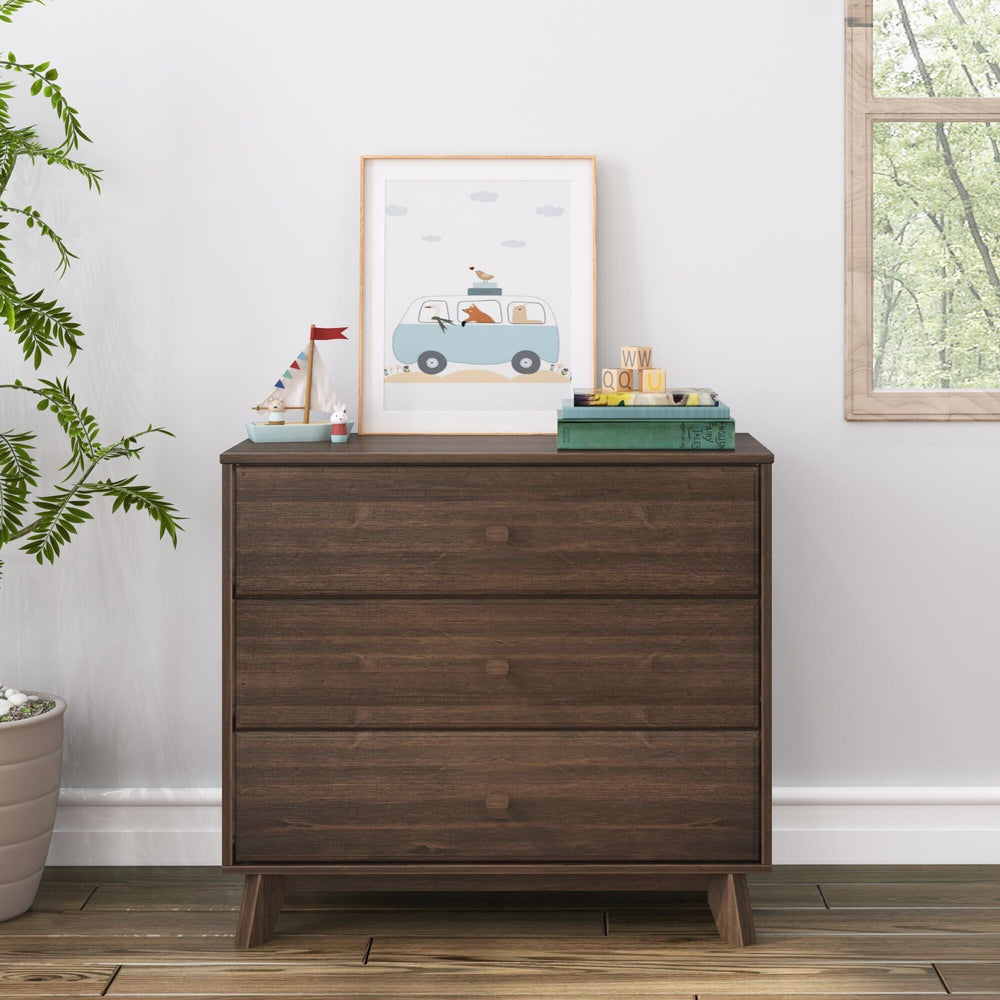 Max & Lily Classic 3 Drawer Dresser in Walnut - shown in a bright room next to a window with framed art and stacked books displayed on top.