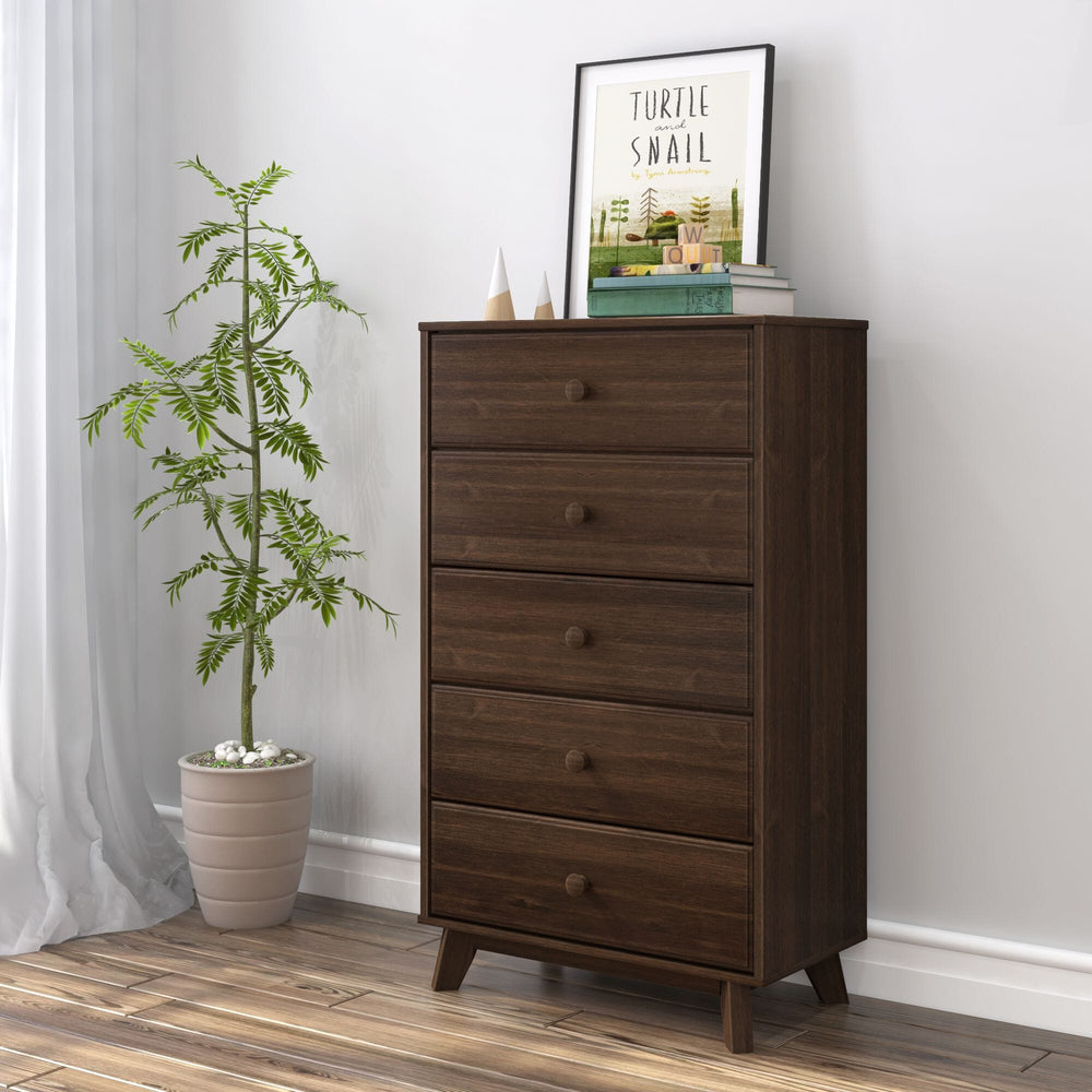 Max & Lily Classic 5 Drawer Dresser in Walnut - angled view styled in a bedroom with a potted plant, framed art, and books on top.