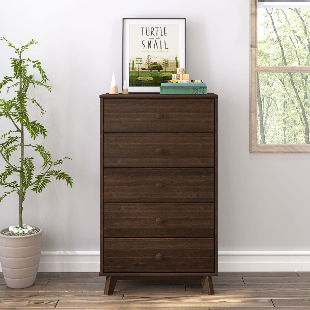 Max & Lily Classic 5 Drawer Dresser in Walnut - front view in a bright bedroom beside a potted plant and window with books and framed art on top.