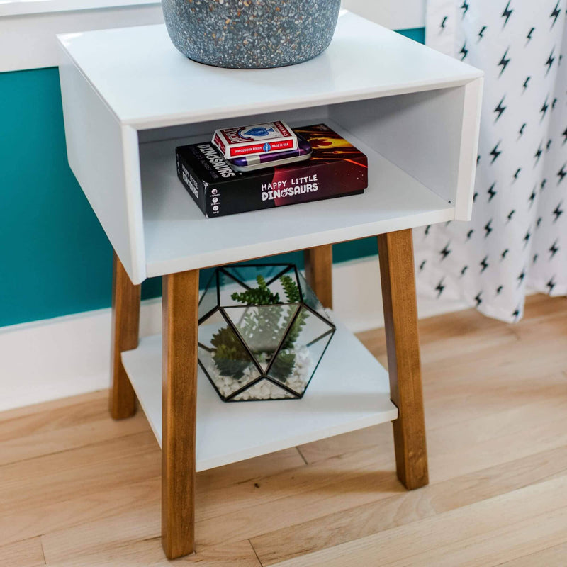 Max & Lily Mid-Century Modern Cubby Night Stand in White/Pecan - close-up of the open cubby compartment holding games and the lower shelf displaying a plant