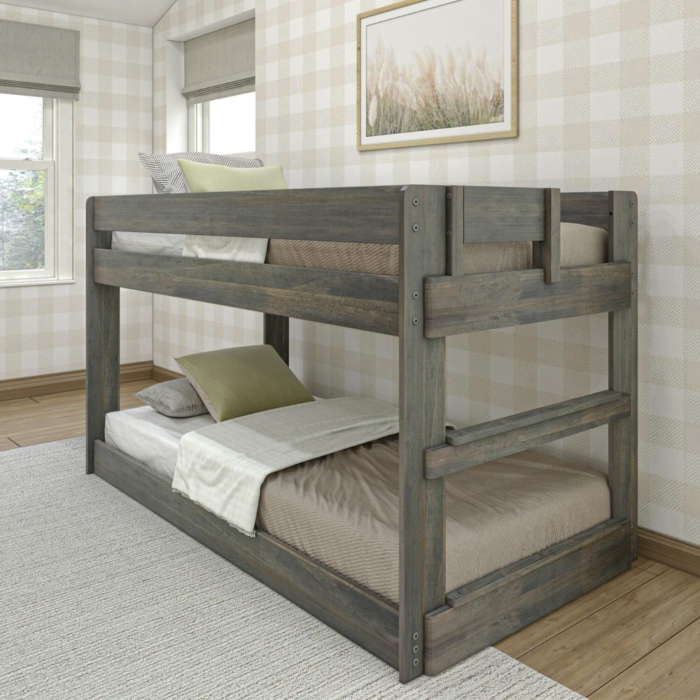 Max & Lily Modern Farmhouse Twin Over Twin Low Bunk Bed in Driftwood - angled view of the low bunk bed with built-in end ladder and safety guardrail in a plaid-wallpapered bedroom.