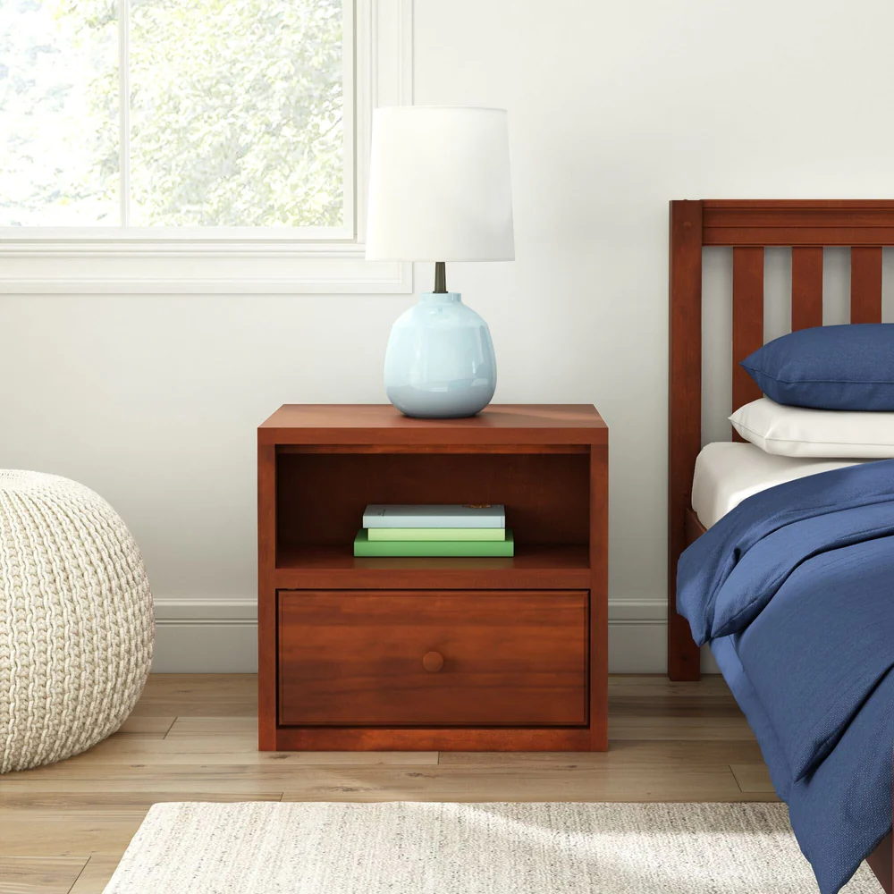 Maxtrix 1 Drawer Nightstand in Chestnut - front view in a bedroom setting next to a bed, with a lamp on top and books tucked in the open shelf