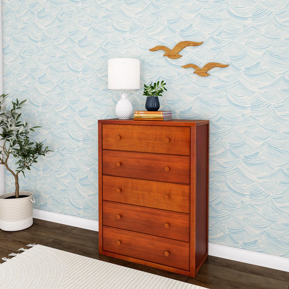 Maxtrix 5 Drawer Dresser Chestnut Angle Room Scene 1 Maxtrix 5 Drawer Dresser in Chestnut - angled view in a kids bedroom with wave-pattern wallpaper, styled with a lamp, plant and books on top