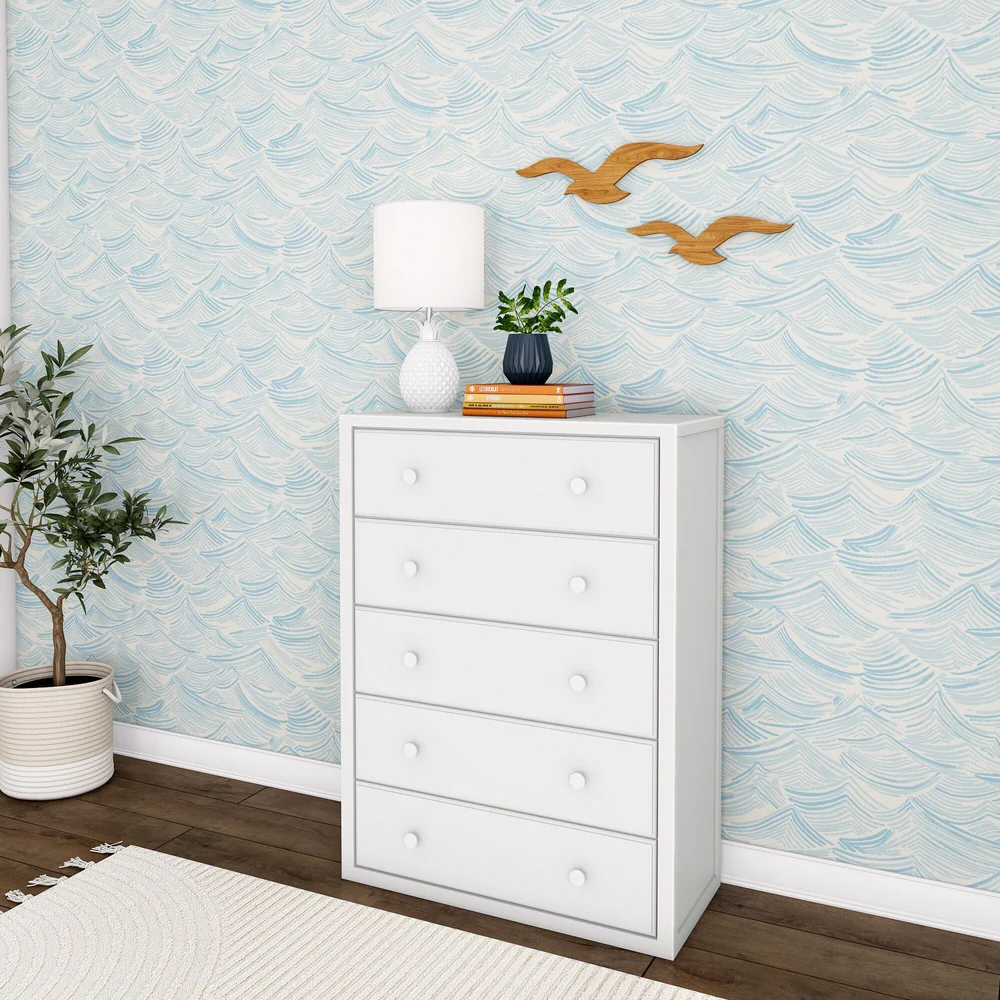 Maxtrix 5 Drawer Dresser White Room Scene Maxtrix 5 Drawer Dresser in White - angled view of the tall five-drawer dresser styled in a kids bedroom with a lamp, plant and books on top against wave-print wallpaper