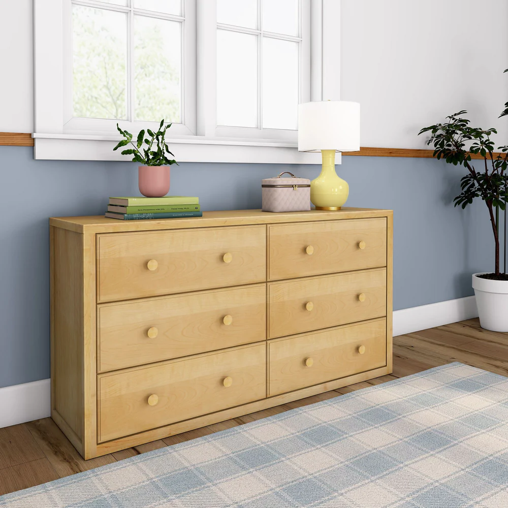 Maxtrix 6 Drawer Dresser in Natural - angled view in a bedroom with a plaid rug and potted plant beside it
