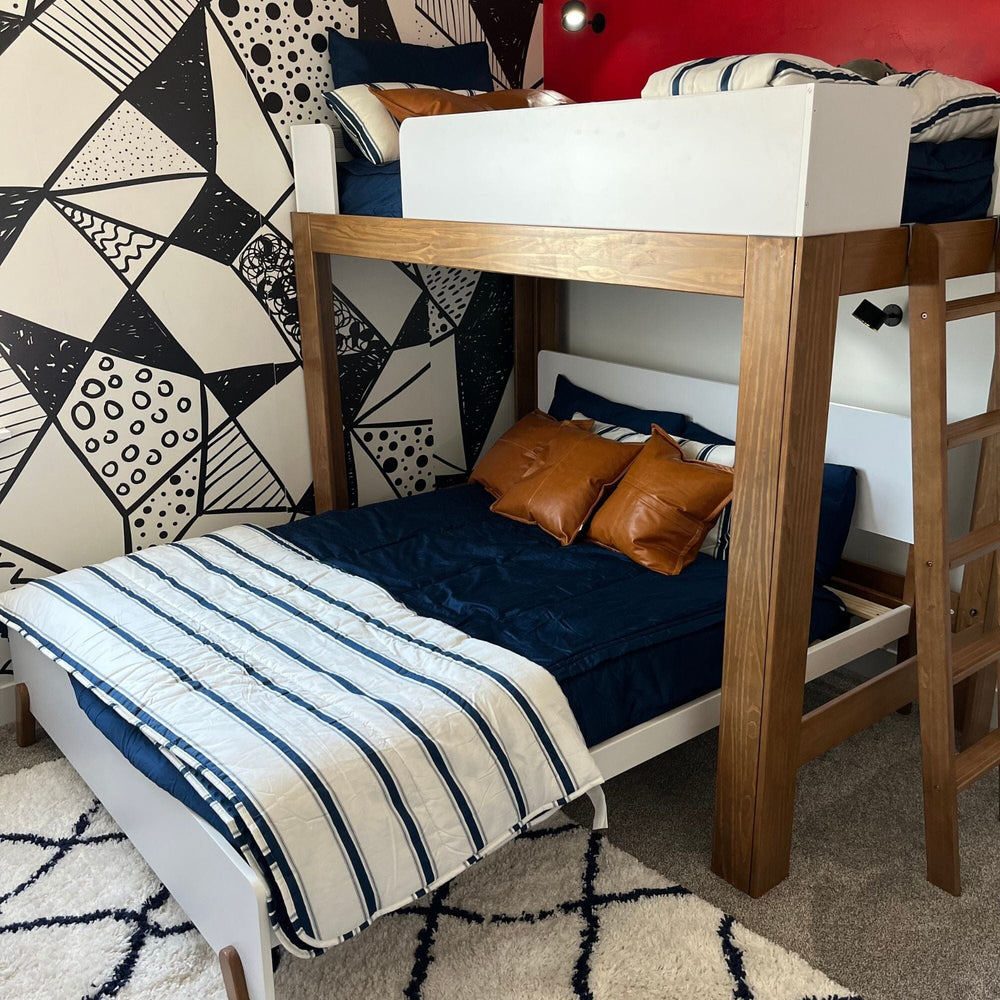 Mid-Century Modern Twin Over Full L-Shaped Bunk Bed in White/Pecan - lifestyle photo in a kids room with navy bedding, showing the lofted twin with guardrails, ladder, and lower full bed