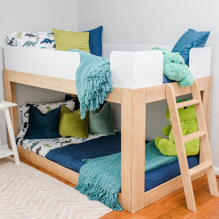 Mid-Century Modern Twin Over Twin Low Bunk Bed in White/Blonde - angled room scene with dinosaur bedding, plush toys, white safety guardrails and angled wood ladder